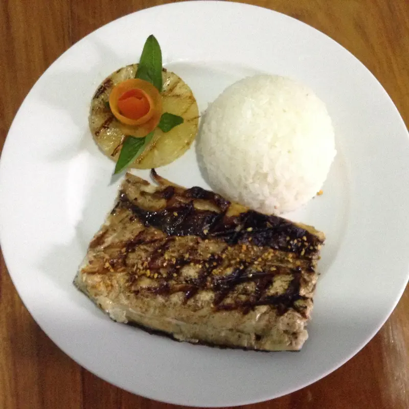 Assiette de poisson grillé accompagné de riz et d'une garniture d'ananas.