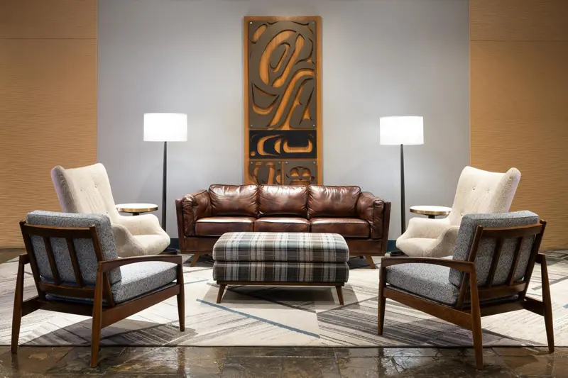 Un salon avec un canapé en cuir brun, deux fauteuils et un pouf.