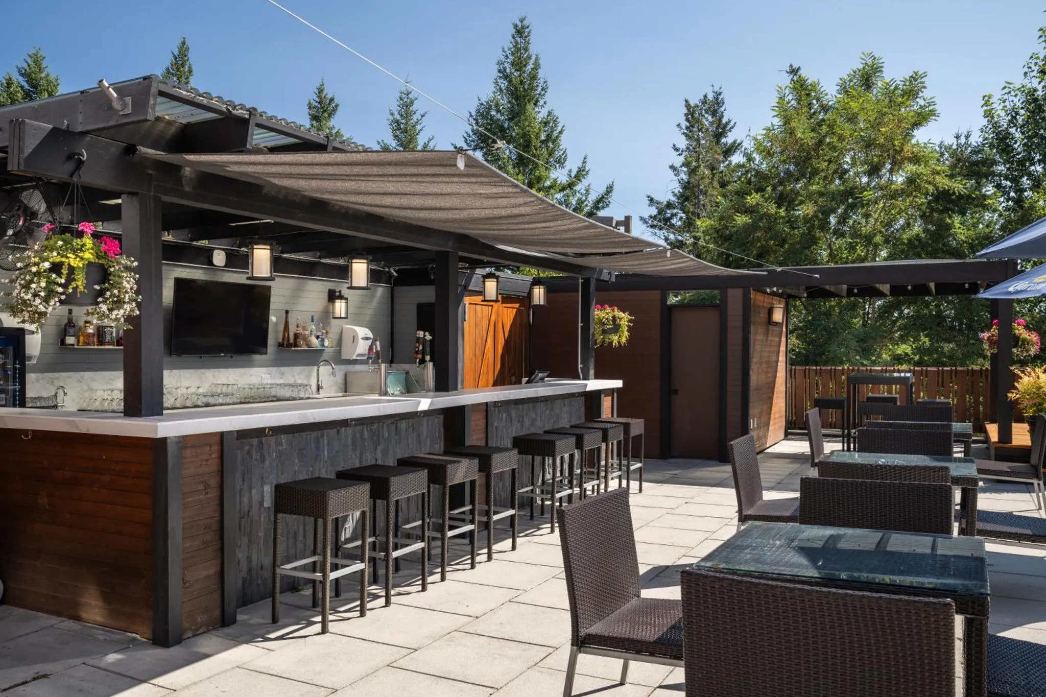 Un bar extérieur avec un comptoir et des tabourets, ainsi que des tables et des chaises sur une terrasse pavée.