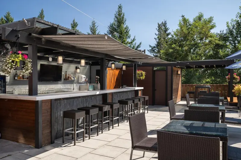 Un bar extérieur avec un comptoir et des tabourets, ainsi que des tables et des chaises sur une terrasse pavée.
