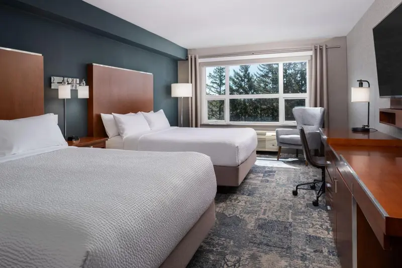 Une chambre d'hôtel avec deux lits et un bureau près d'une fenêtre.