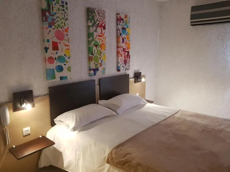 Une chambre avec un lit double et des tableaux colorés au mur.