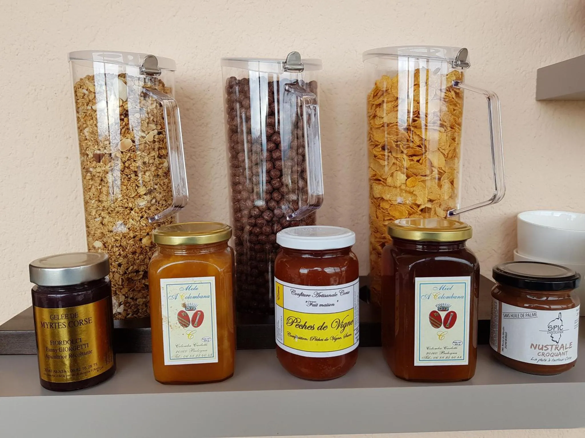 Des bocaux de céréales, de muesli et de confitures sont alignés sur une étagère.