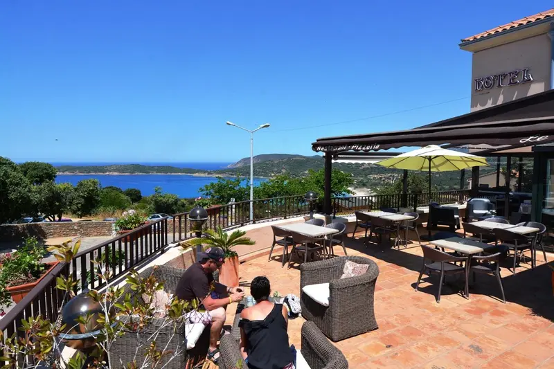 Terrasse ombragée avec tables et chaises donnant sur une vue côtière.