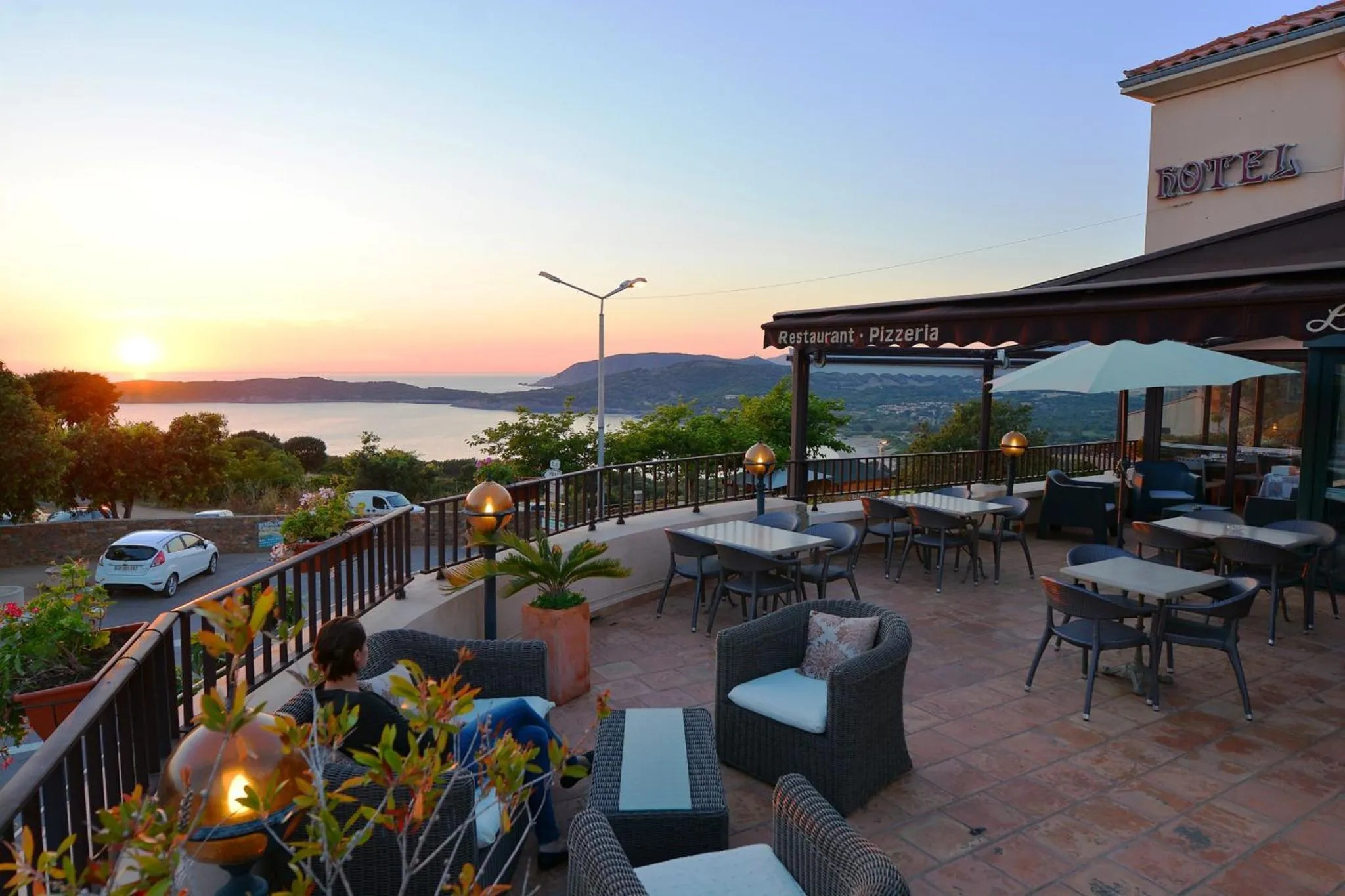 Terrasse avec tables et chaises offrant une vue sur la mer au coucher du soleil.