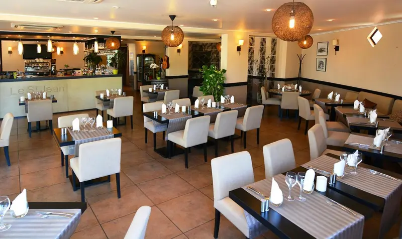 Une salle de restaurant lumineuse avec des tables dressées et des luminaires décoratifs.