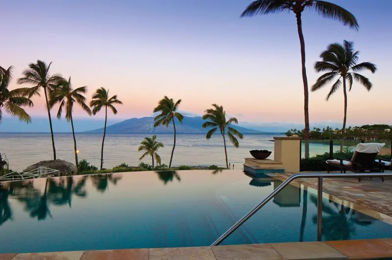 Une piscine à débordement offre une vue sur la mer et les montagnes au coucher du soleil.