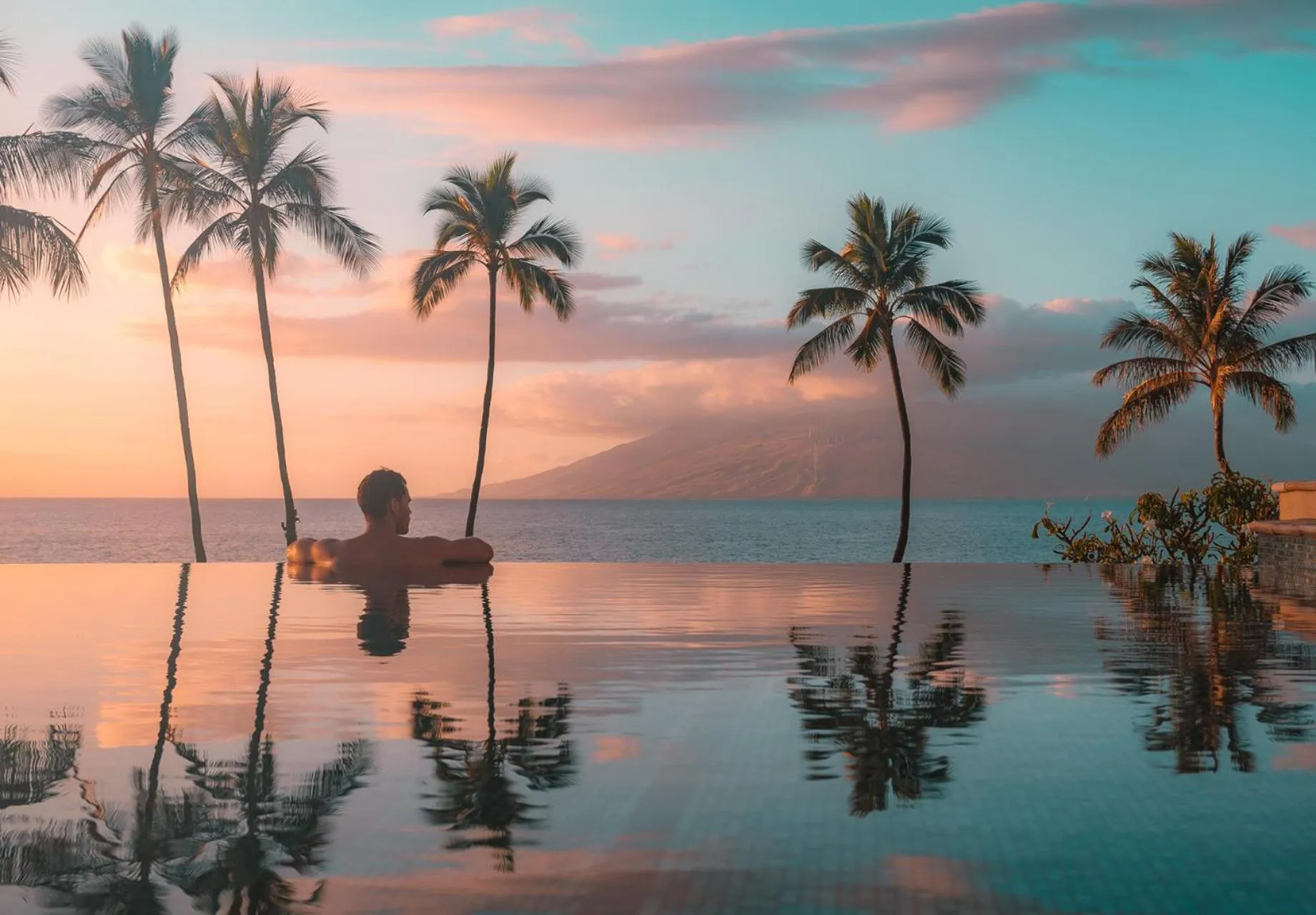 Une personne se détend dans une piscine à débordement face à la mer au coucher du soleil.