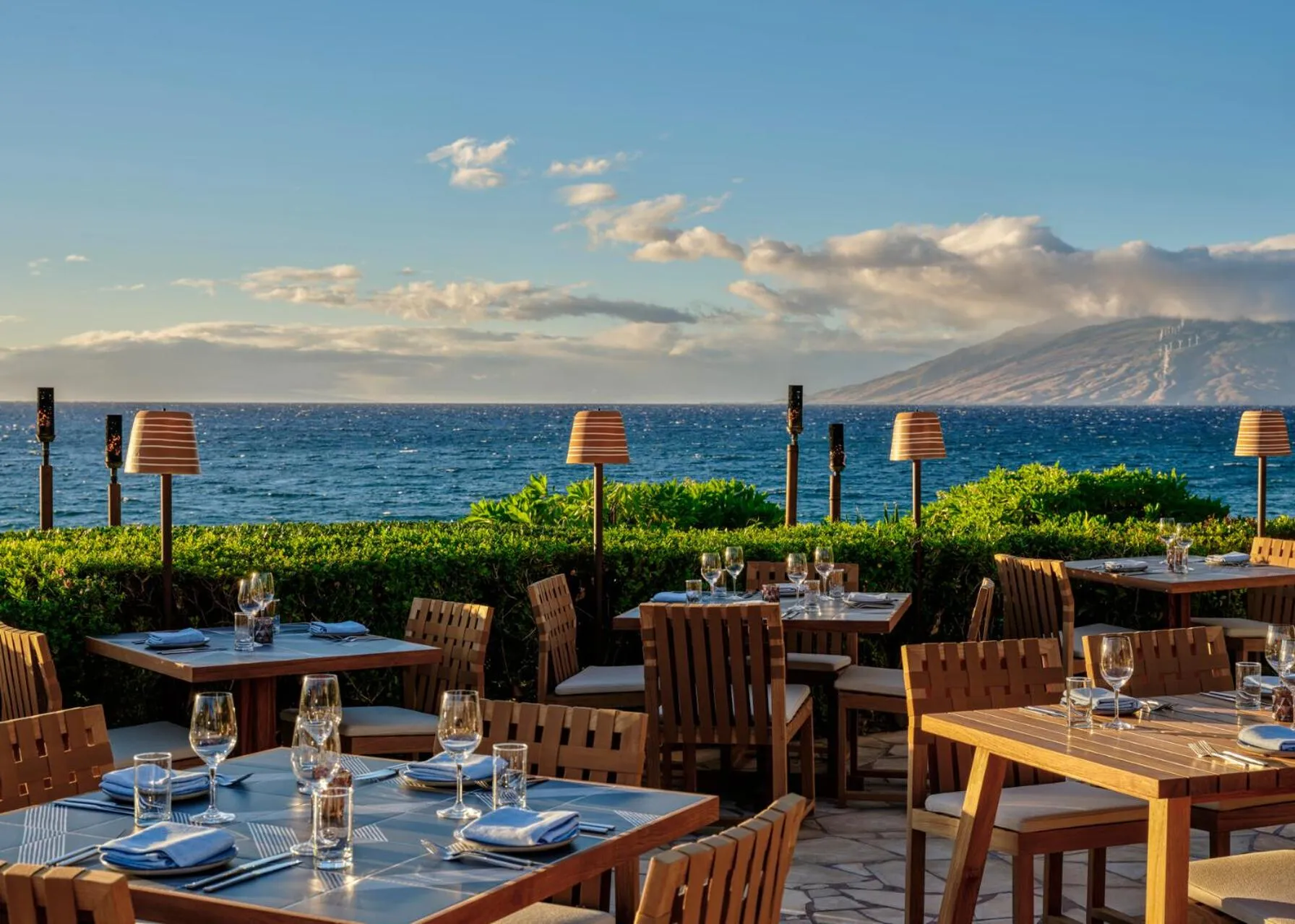 Tables de restaurant en extérieur avec vue sur la mer et les montagnes.