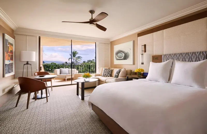Une chambre lumineuse avec un grand lit et un coin salon donnant sur une vue extérieure.