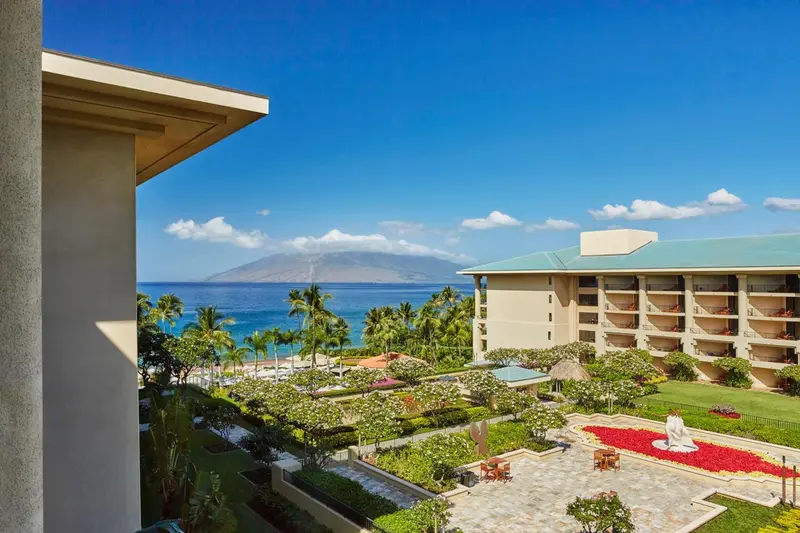 Vue d'un jardin luxuriant et d'une mer bleue depuis un balcon.