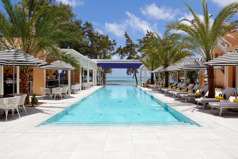 Une longue piscine rectangulaire bordée de transats et de parasols rayés.