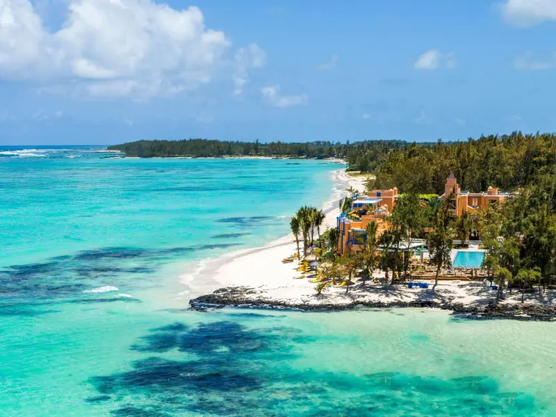 Vue aérienne d'une plage de sable blanc bordée d'eau turquoise et de végétation luxuriante.
