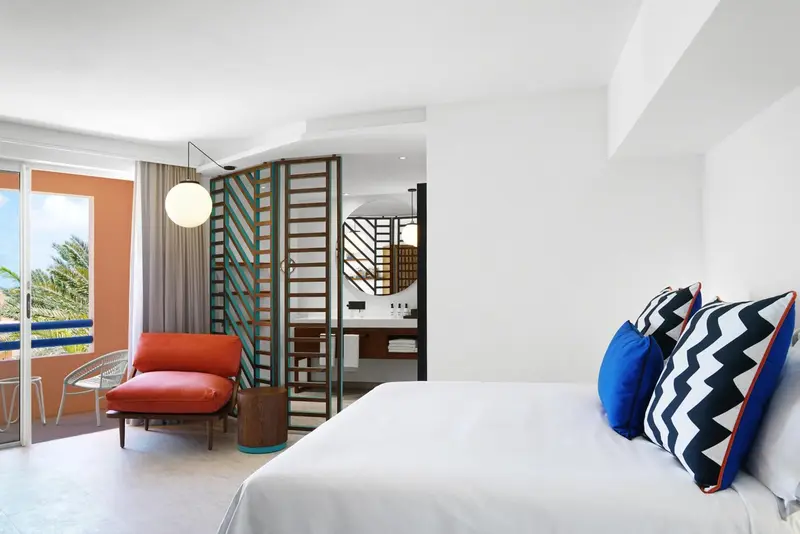Chambre lumineuse avec un lit blanc et un fauteuil rouge.