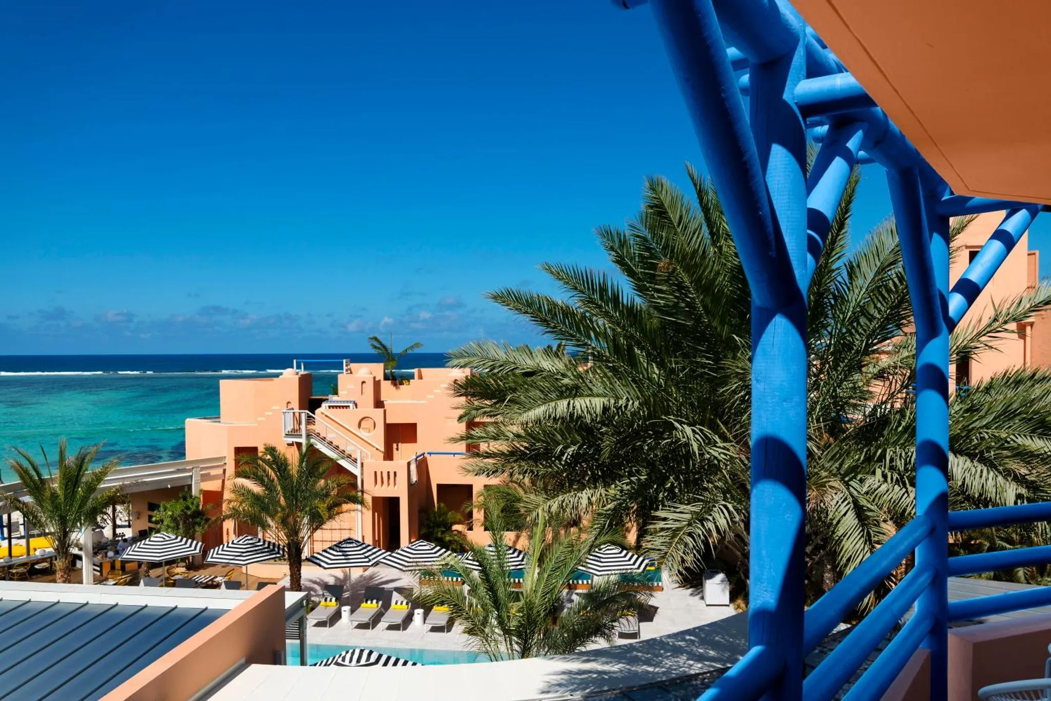 Vue d'un complexe hôtelier avec piscine et végétation tropicale face à la mer.