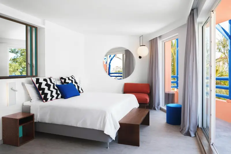Une chambre lumineuse avec un lit fait et un accès à un balcon coloré.