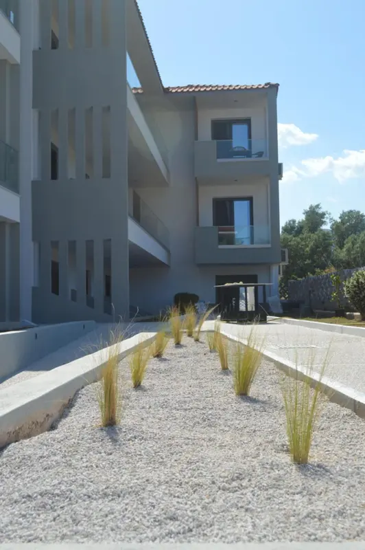 Façade d'un bâtiment moderne avec des arbustes devant un sol gravillonné.