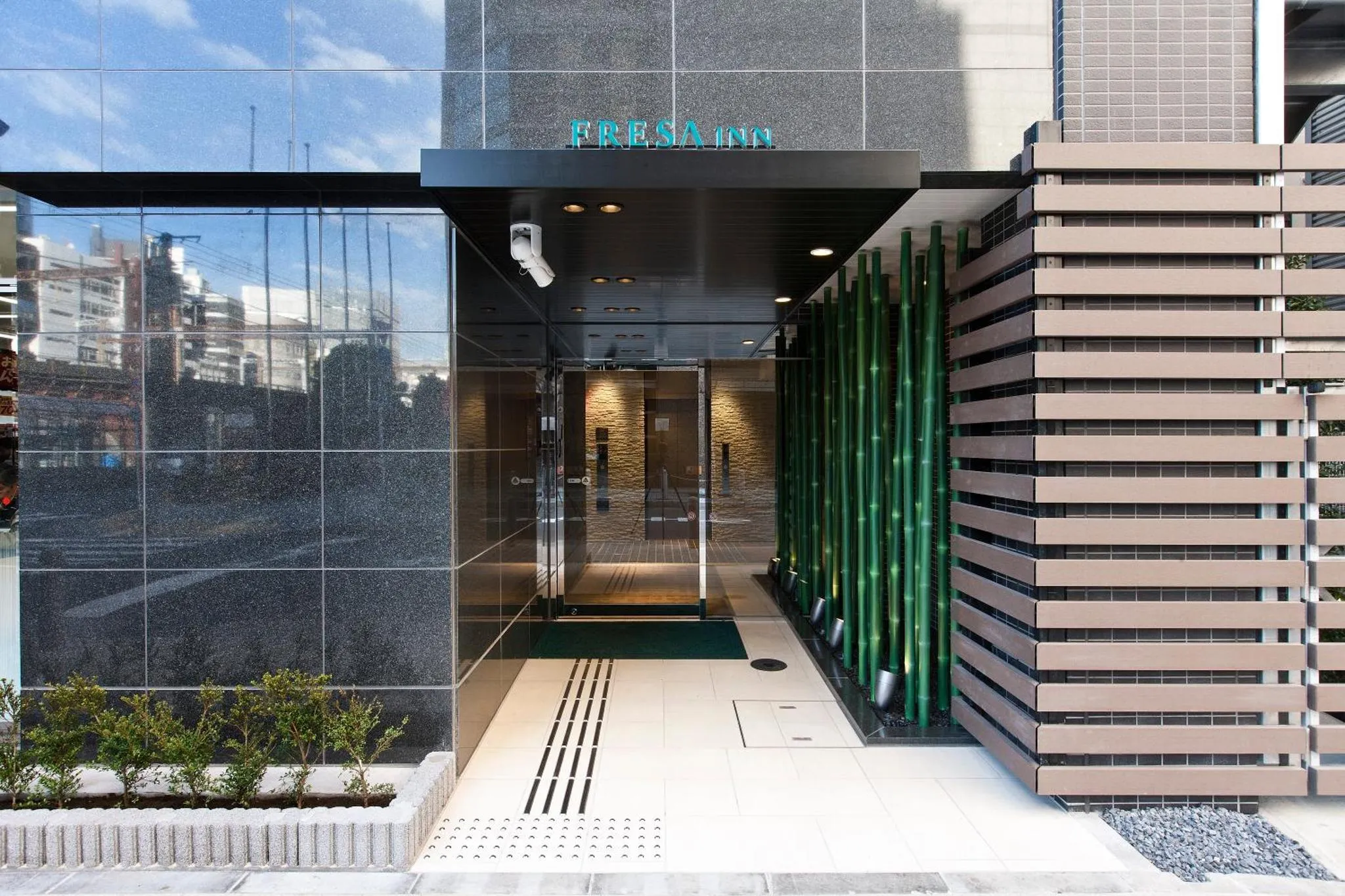 Entree d'un batiment moderne avec facade en verre et elements decoratifs verts.