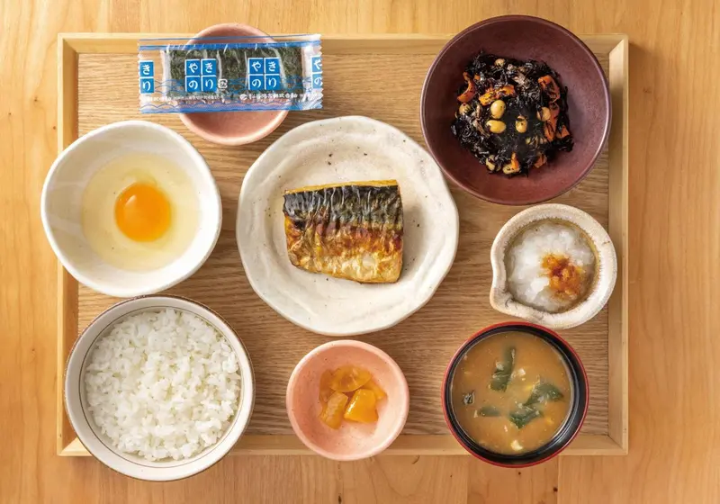 Un plateau en bois présente un petit-déjeuner japonais avec riz, poisson grillé et plusieurs accompagnements.