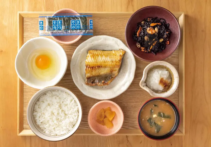 Un plateau en bois présente un petit-déjeuner japonais avec riz, poisson grillé et accompagnements.
