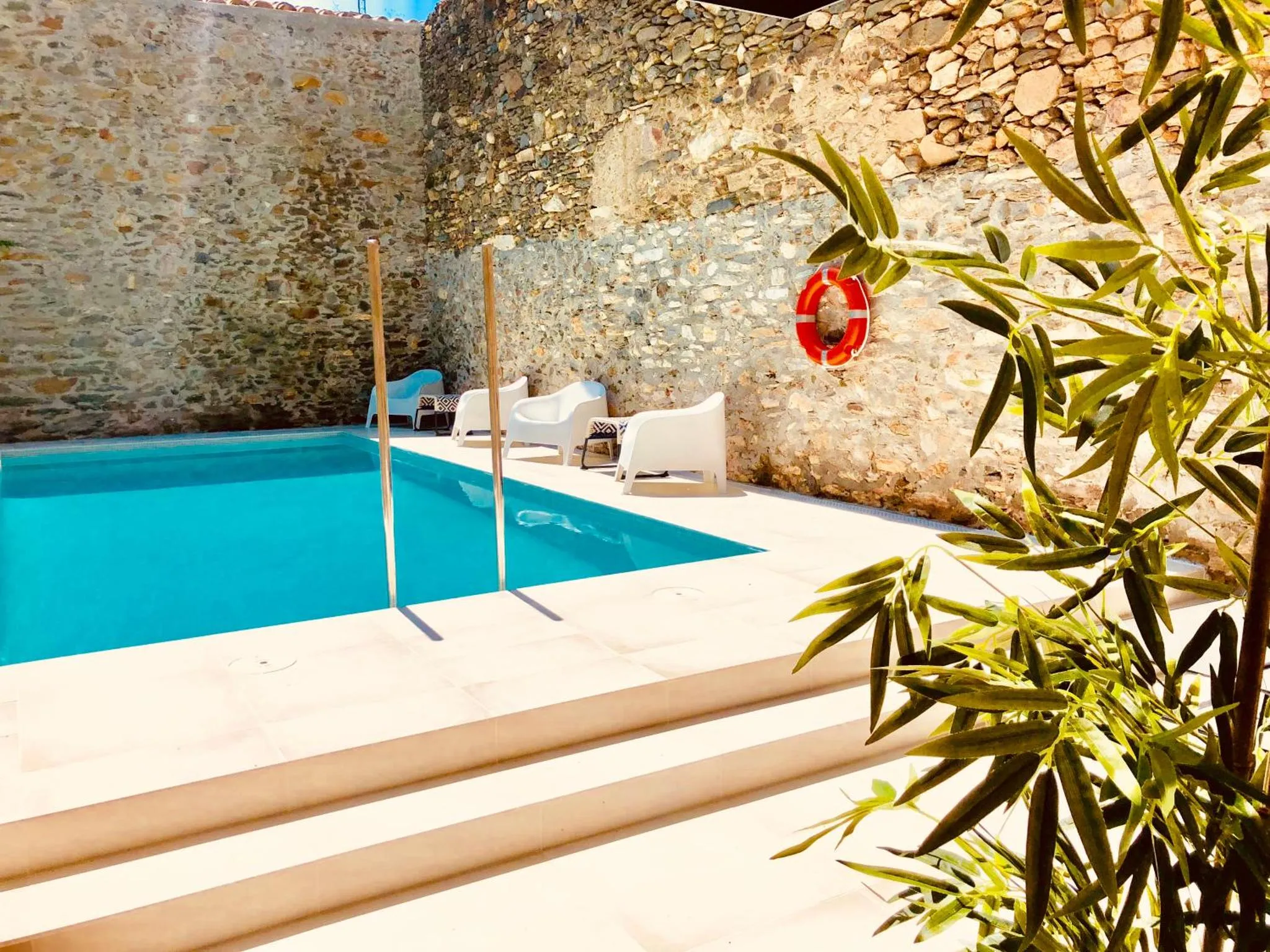 Une piscine rectangulaire bordée de chaises longues blanches et d'une terrasse ensoleillée.