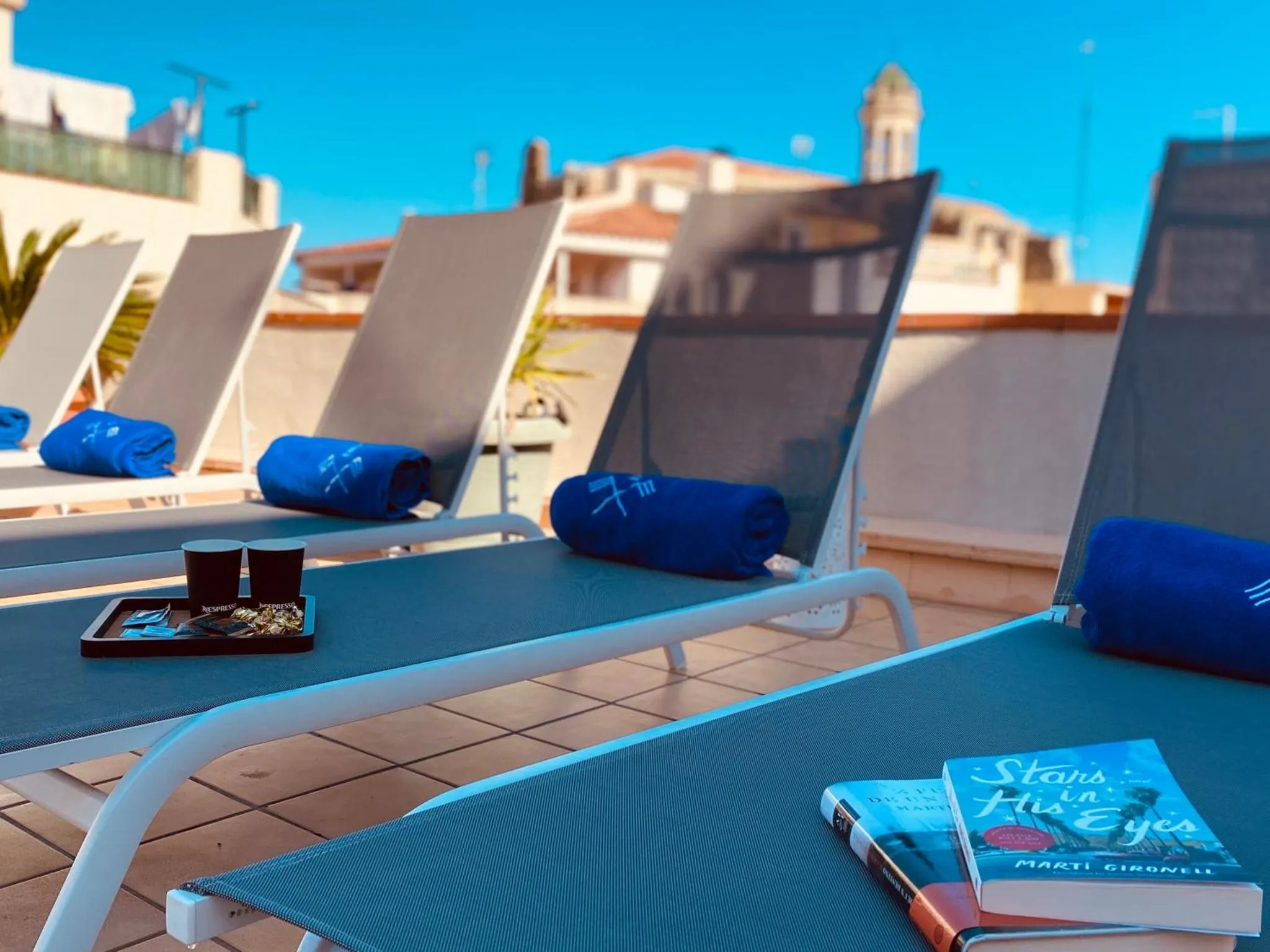 Transats bleus alignés sur une terrasse ensoleillée avec des serviettes et des livres.