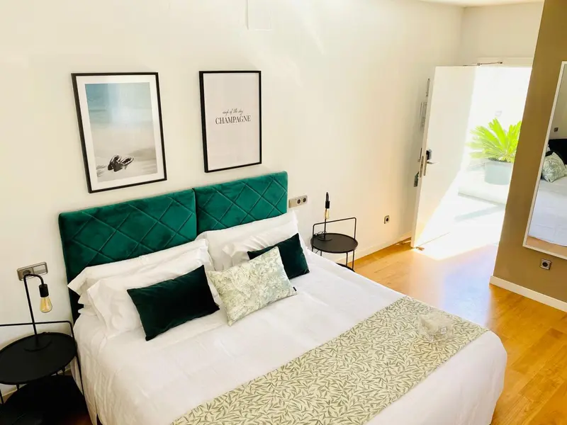 Une chambre lumineuse avec un grand lit recouvert d'une tête de lit verte et de coussins décoratifs.