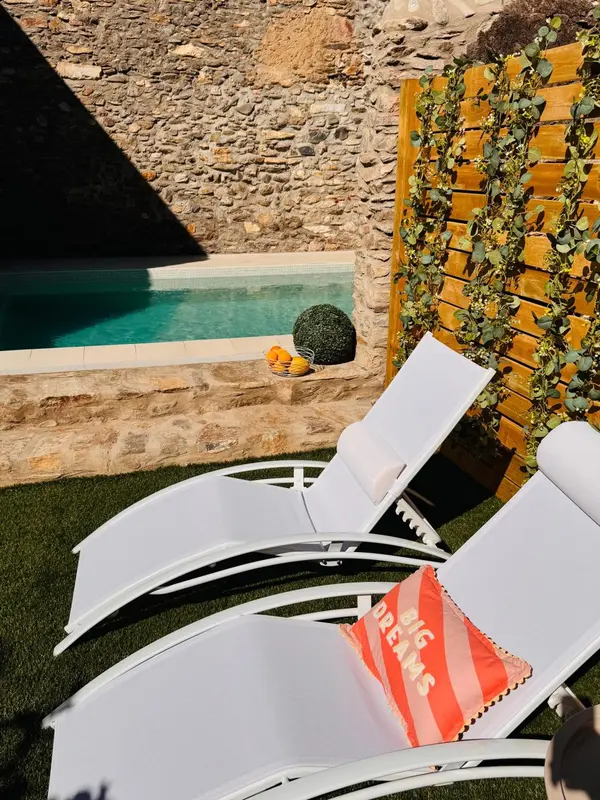 Transats blancs disposés devant une piscine turquoise dans un jardin soigné.