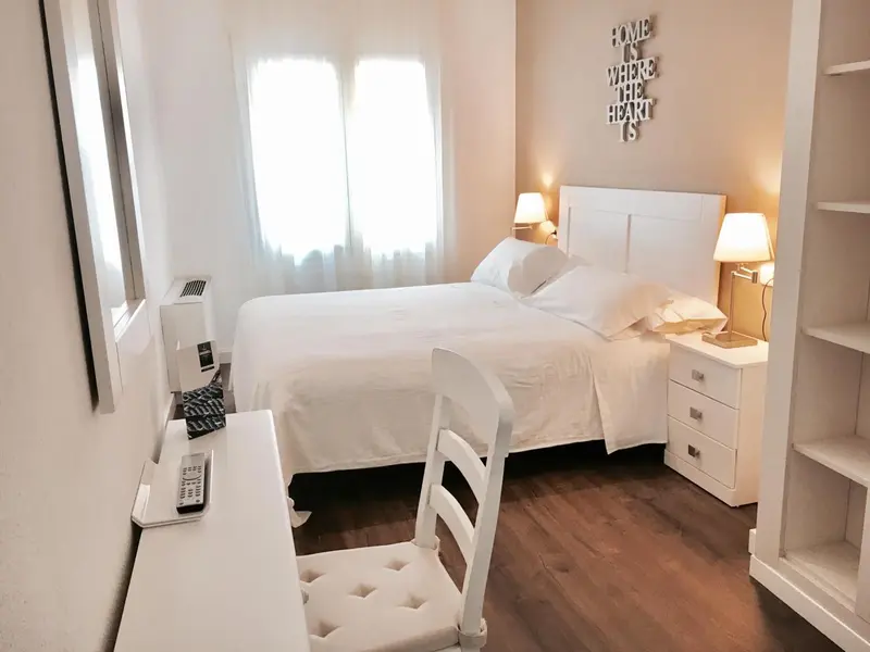 Une chambre lumineuse avec un lit blanc et un bureau.