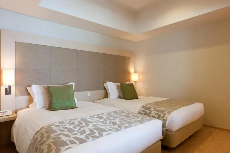 Une chambre lumineuse avec deux lits simples et des coussins verts.