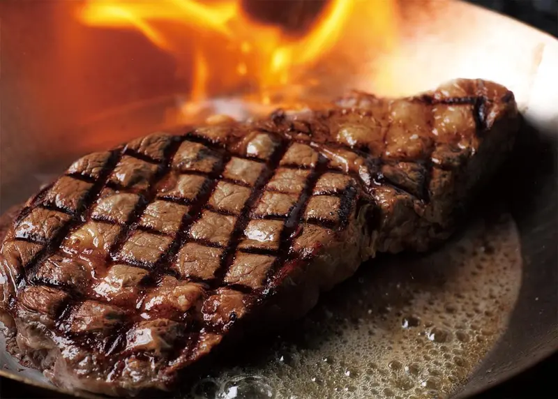 Une viande grillée cuit dans une poêle avec des flammes.