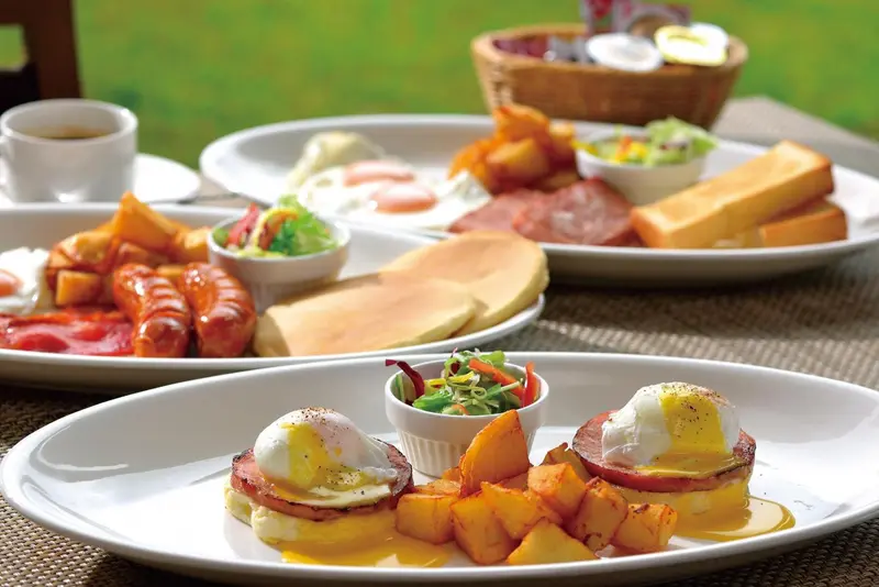 Une table est dressée avec un copieux petit-déjeuner composé de fruits, d'œufs, de saucisses et de viennoiseries.