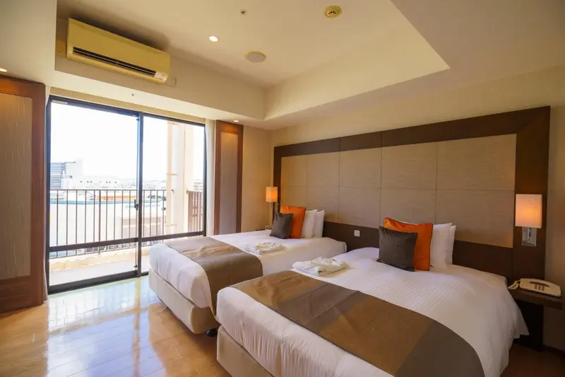 Chambre lumineuse avec deux lits simples et balcon.