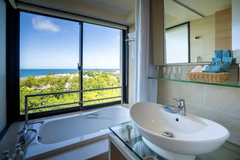 Une baignoire et un lavabo dans une salle de bain lumineuse avec vue sur la mer.
