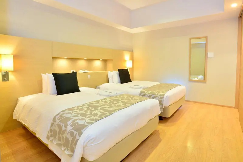 Une chambre lumineuse avec deux lits simples et un grand miroir.