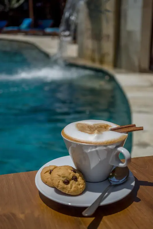Une tasse de café et des biscuits sont posés sur une table près d'une piscine.