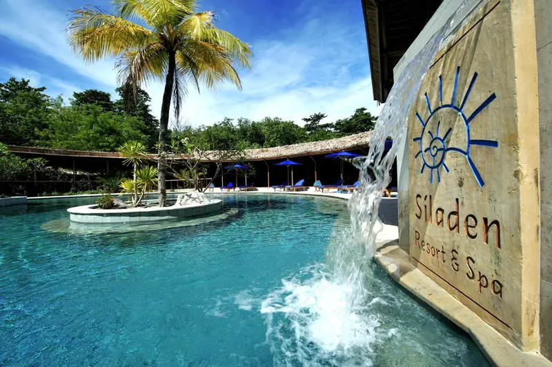 Une piscine turquoise bordée de végétation luxuriante et de chaises longues.