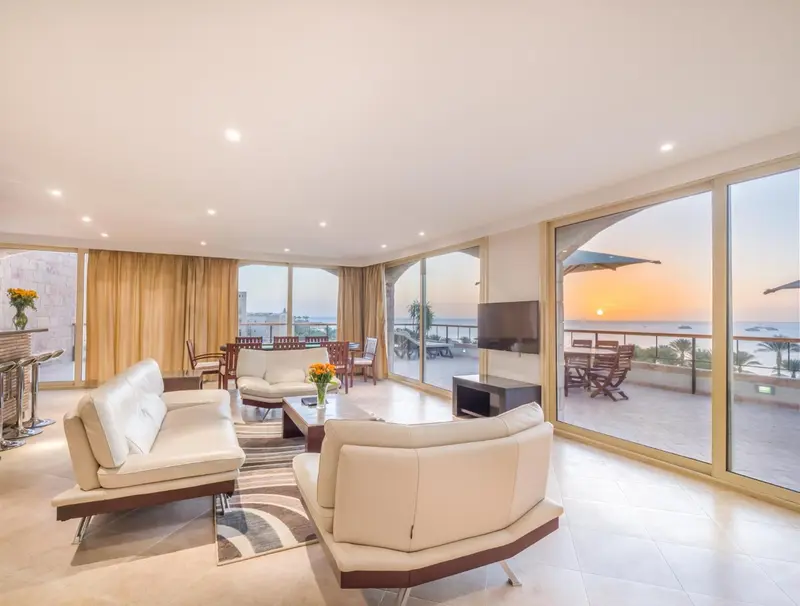 Un salon lumineux s'ouvre sur une terrasse avec vue sur la mer au coucher du soleil.