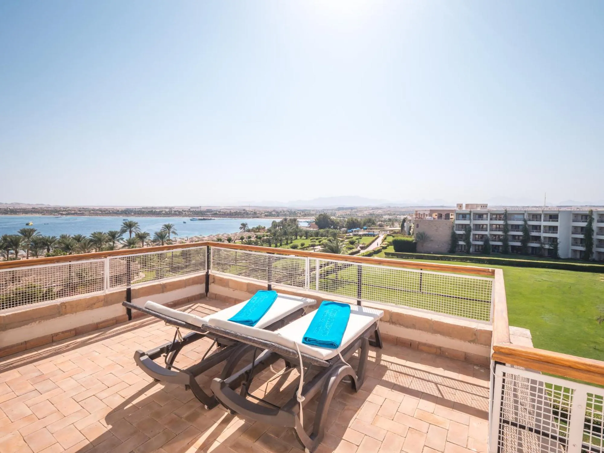 Deux transats bleus sur une terrasse carrelée avec vue sur la mer et la ville.