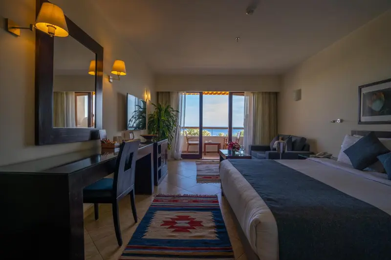 Une chambre spacieuse avec un lit et un coin salon donnant sur une vue mer.