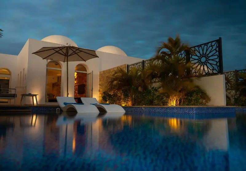 Deux chaises longues blanches bordent une piscine illuminée au crépuscule.