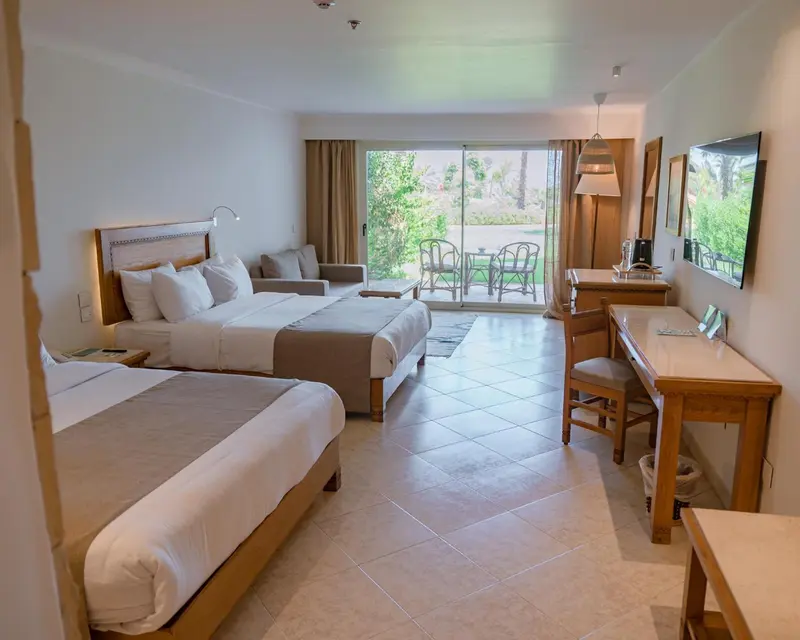 Une chambre lumineuse avec un grand lit et un coin salon donnant sur une terrasse.