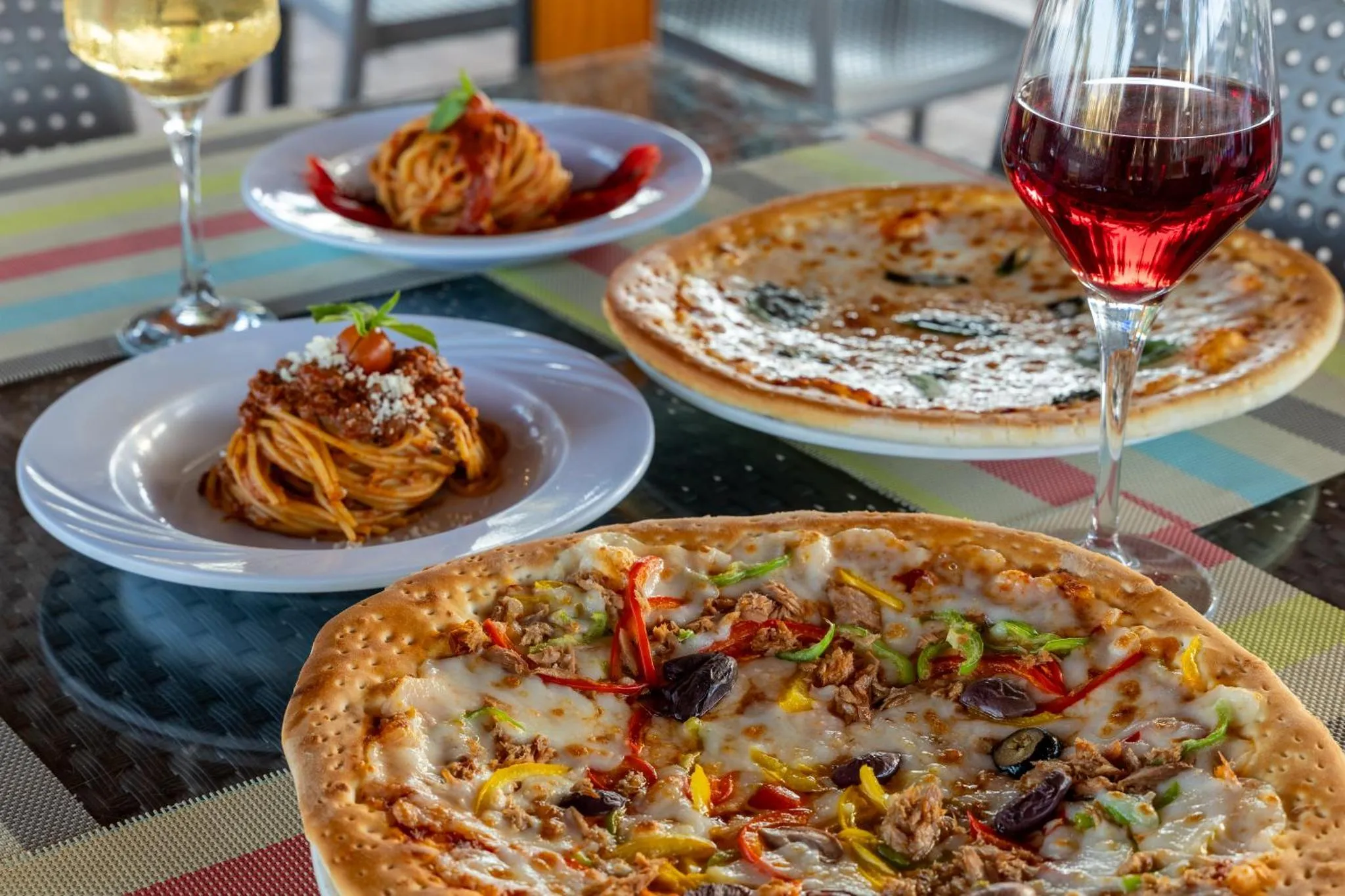 Assiettes de pâtes et de pizzas accompagnées de verres de vin sur une table.