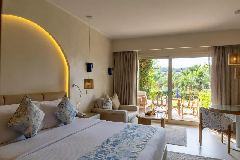 Chambre lumineuse avec un grand lit et un accès à une terrasse.