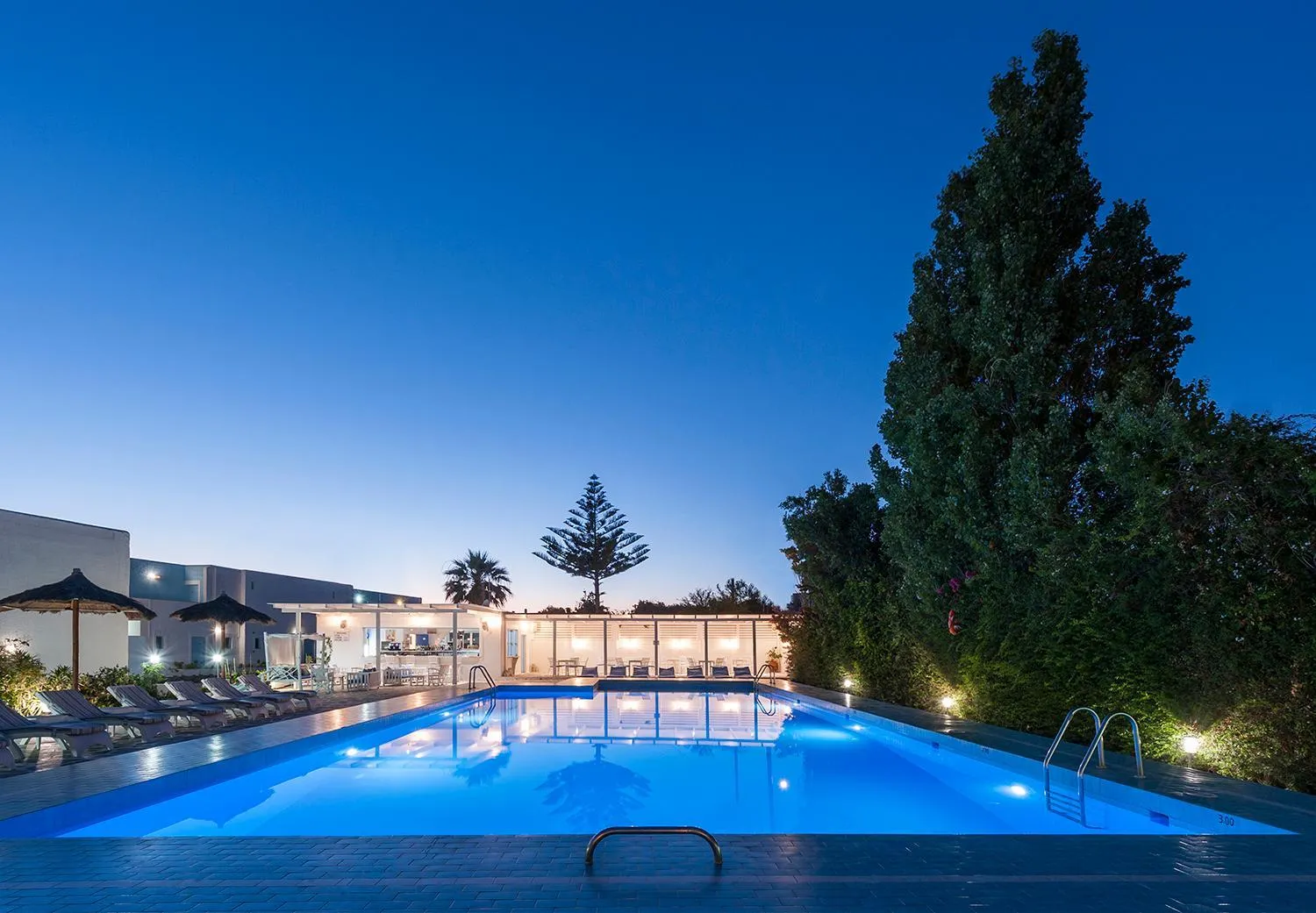 Piscine illuminée au crépuscule avec bâtiments en arrière-plan.