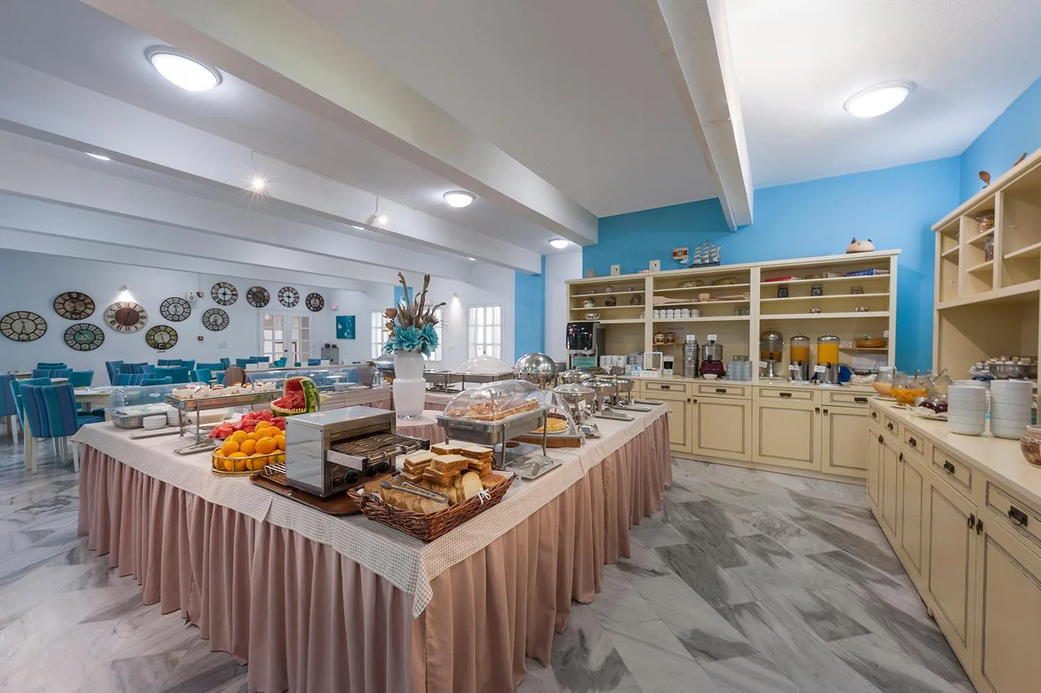 Un buffet propose des fruits, des viennoiseries et des boissons dans une salle lumineuse.
