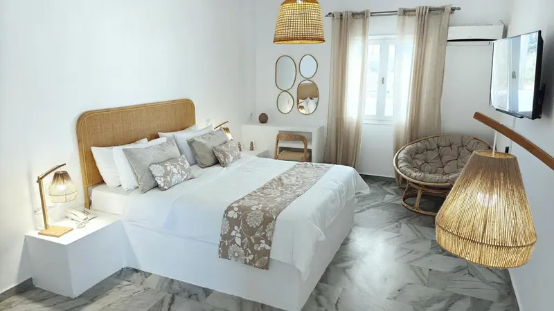 Une chambre lumineuse avec un grand lit et un fauteuil en rotin.