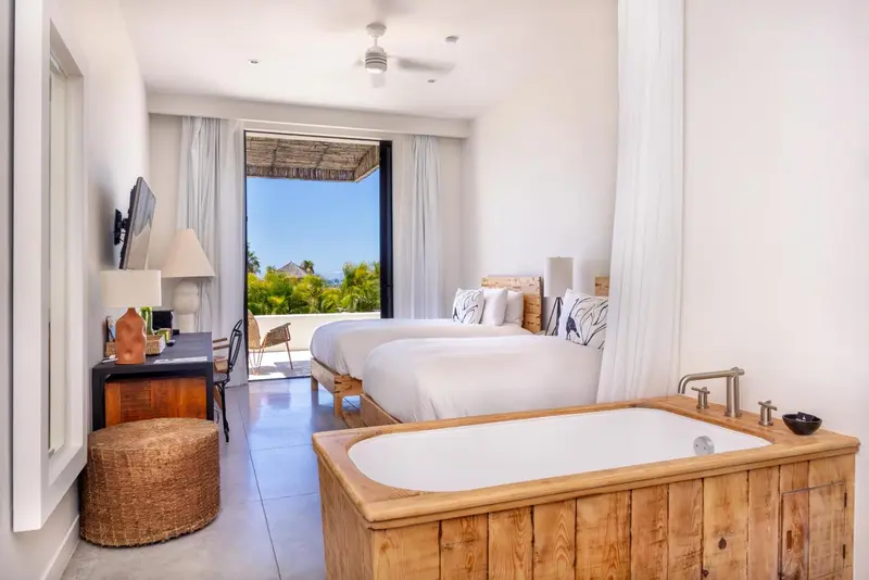Chambre lumineuse avec lit double et baignoire, donnant sur une vue extérieure.