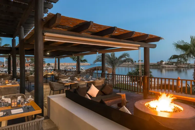 Terrasse aménagée avec salon et tables de repas face à la mer.