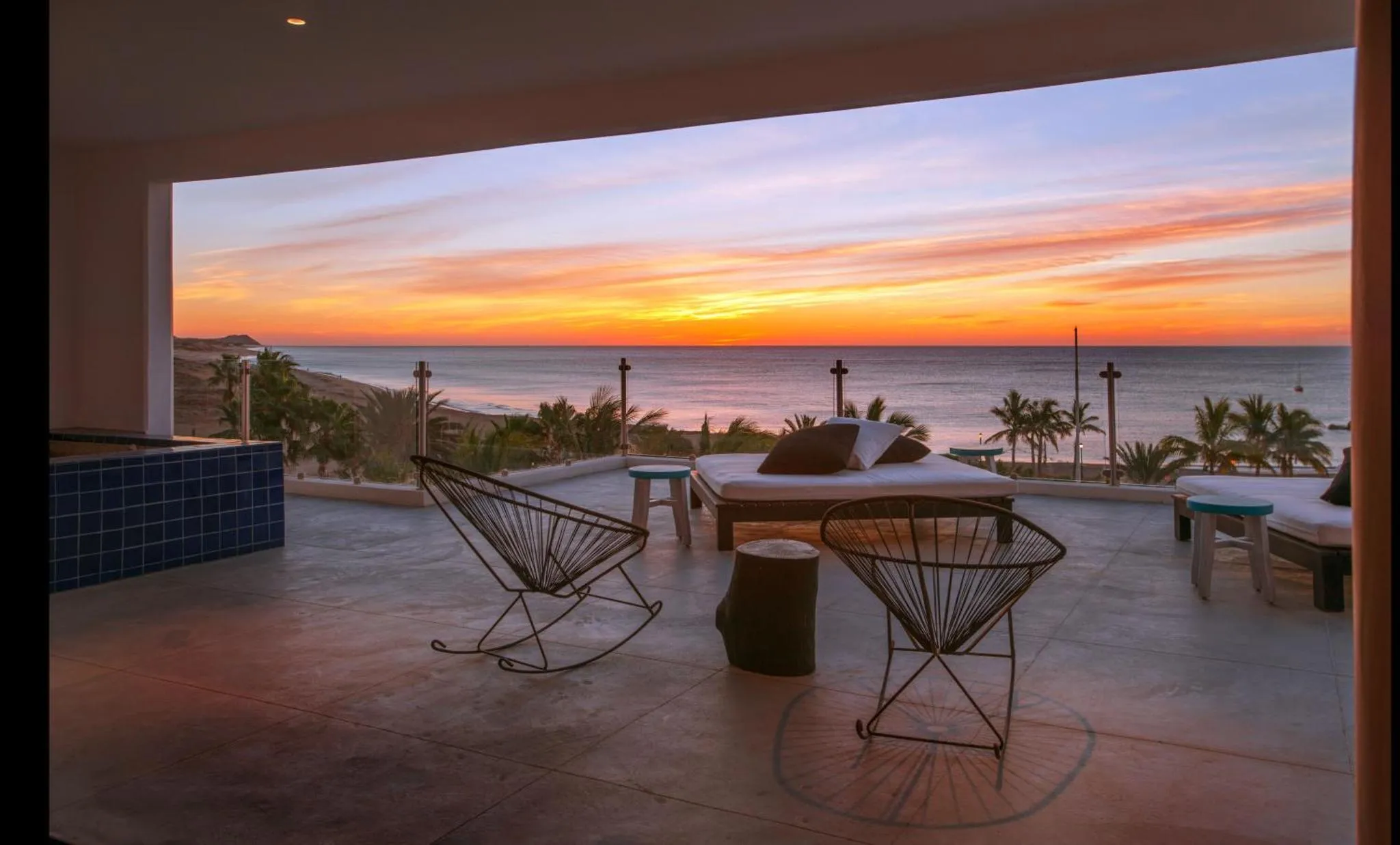 Terrasse aménagée avec chaises et transats face à la mer au coucher du soleil.